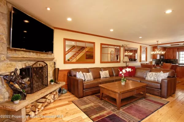 Living room with a stone fireplace, brown leather sectional, and warm wood floors.