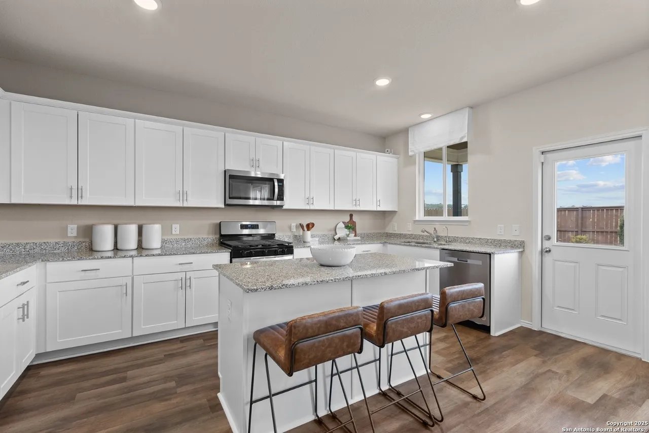 Bright kitchen with white cabinets, granite counters, stainless appliances, and an island with three brown stools.