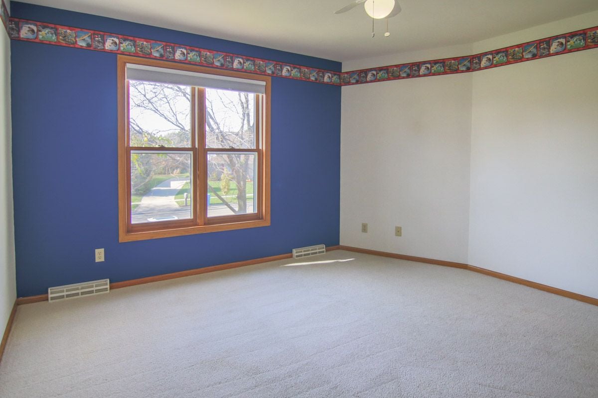 Vacant bedroom with a blue accent wall, wood-trimmed window, and patterned border.