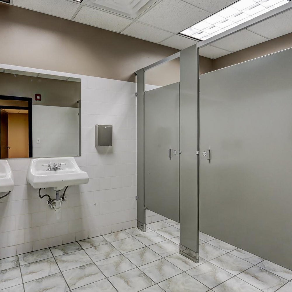 Commercial restroom with gray stall partitions, wall-mounted sinks, and marbled tile flooring.