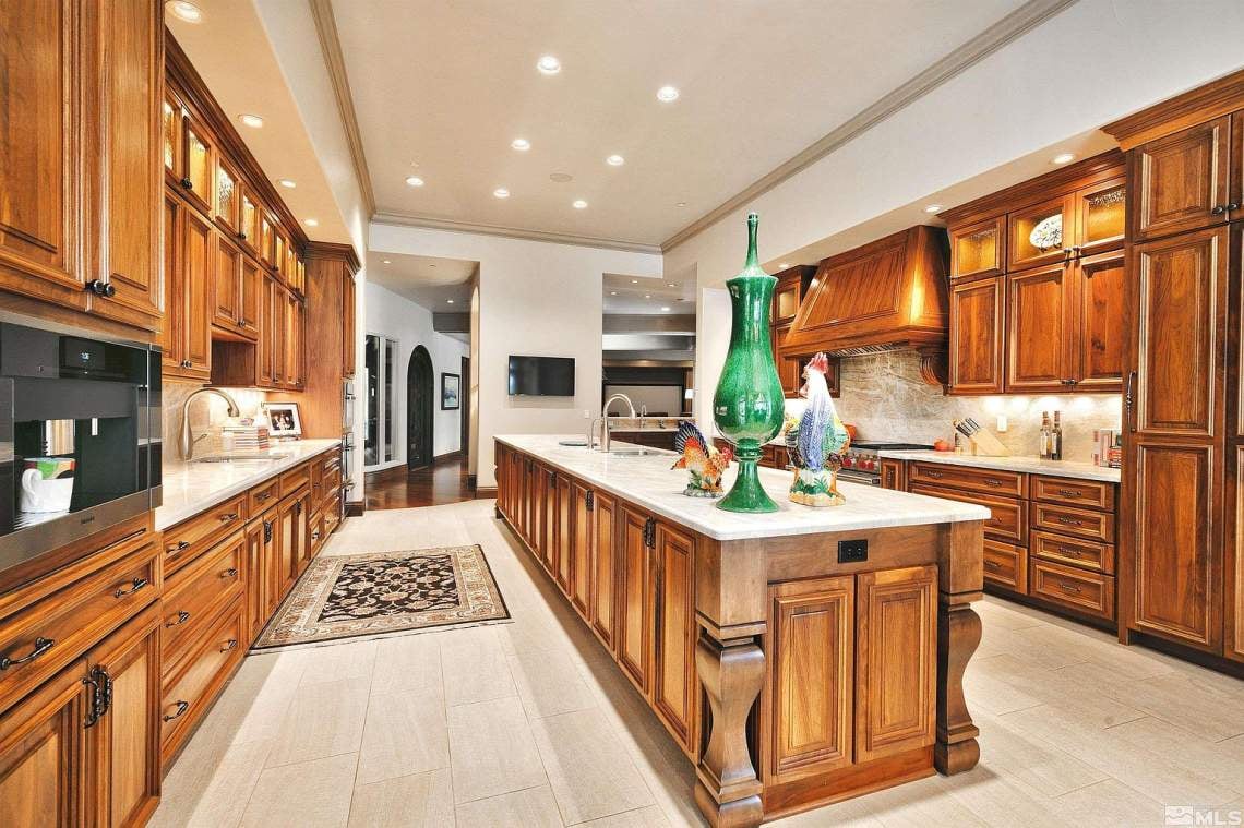 Luxury kitchen with warm wood cabinetry, a large island, pale stone counters, and a green glass vase.