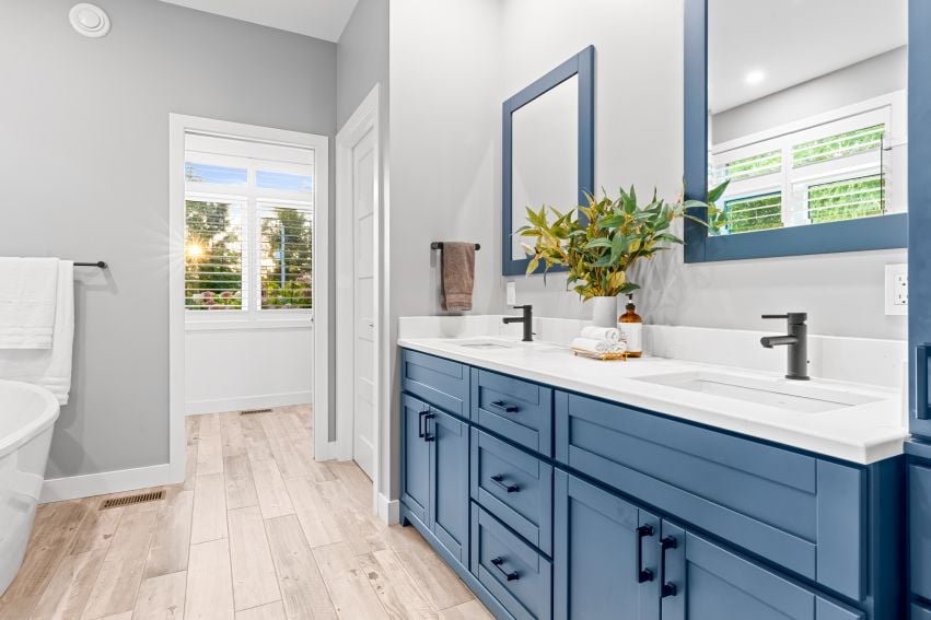 Bright bathroom with a long blue double vanity, white counters, and part of a freestanding tub.