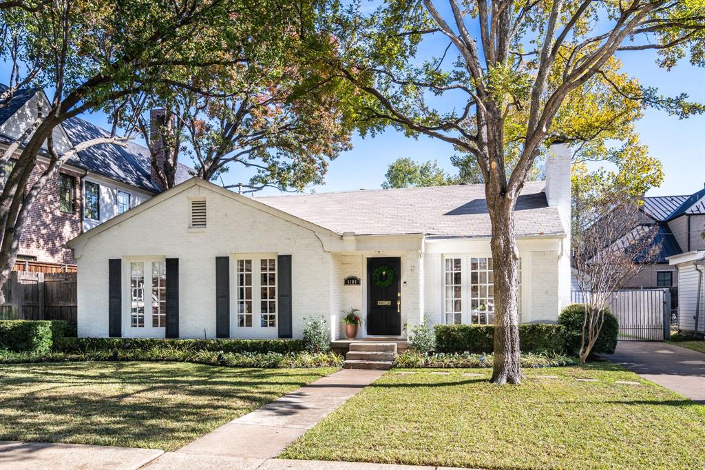 White brick home with black shutters, a dark front door, and mature trees in the front yard.