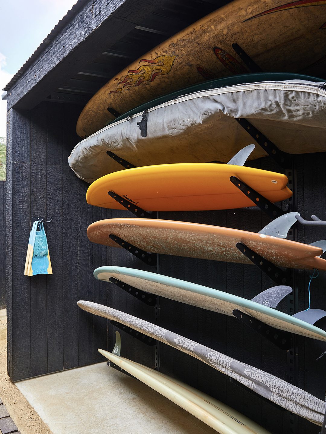 A custom wall-mounted surfboard rack holding several surfboards, built into a black-painted exterior wall.