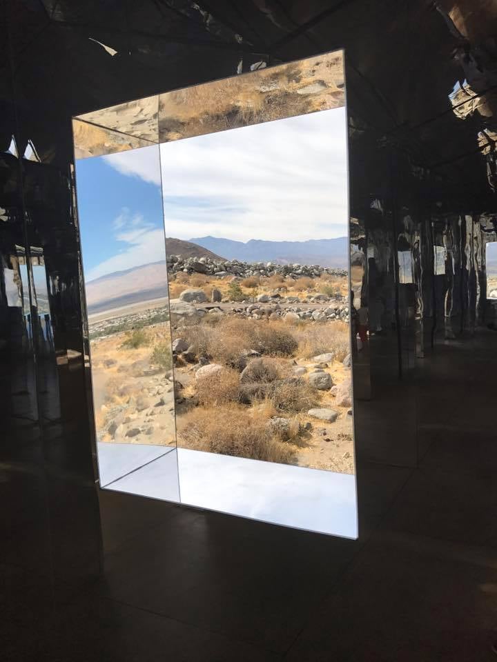 Mirage installation frames a rocky desert landscape through a large mirrored opening.