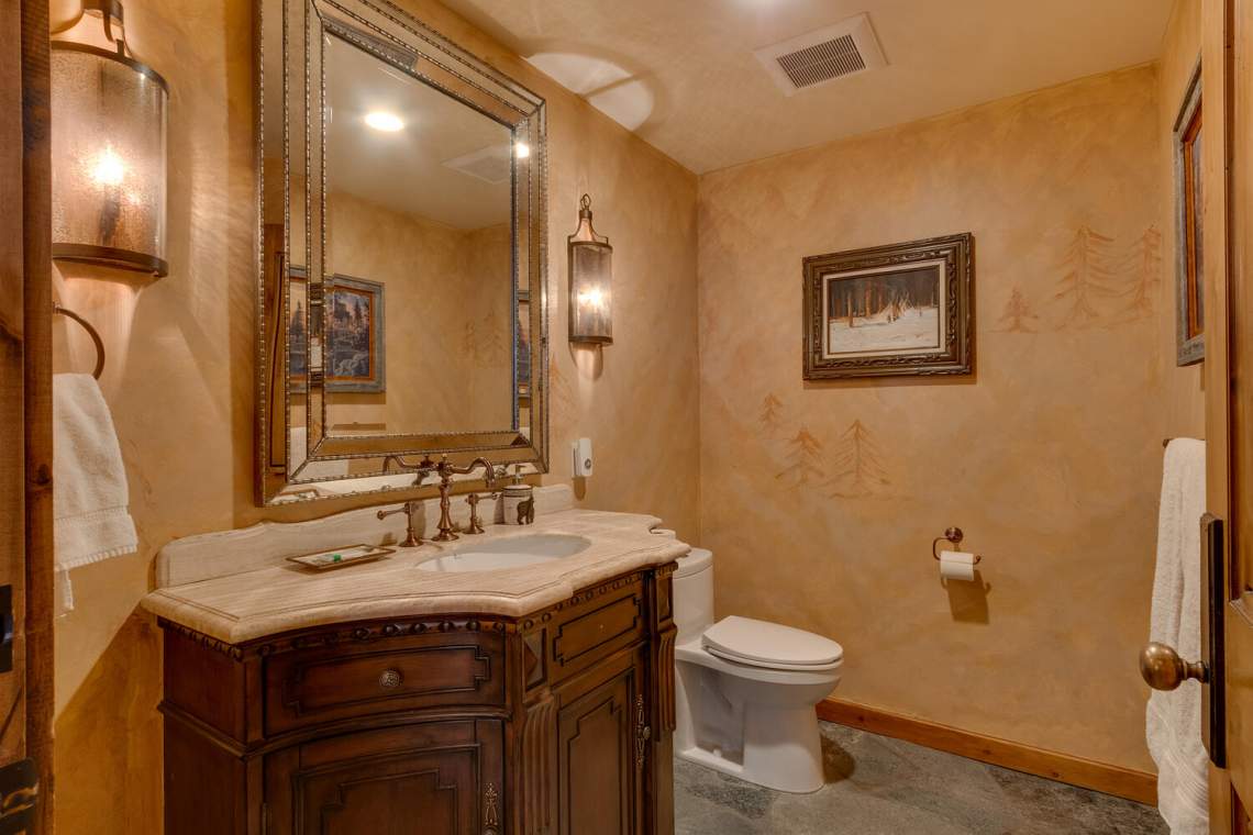 Bathroom with a dark wood vanity, cream stone countertop, large mirror, and framed artwork.