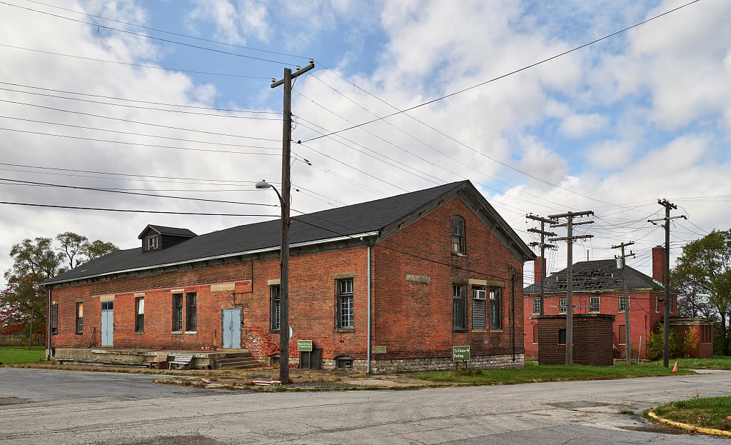 Red-brick industrial building with a dark gabled roof, street-level loading platform, and overhead utility wires.