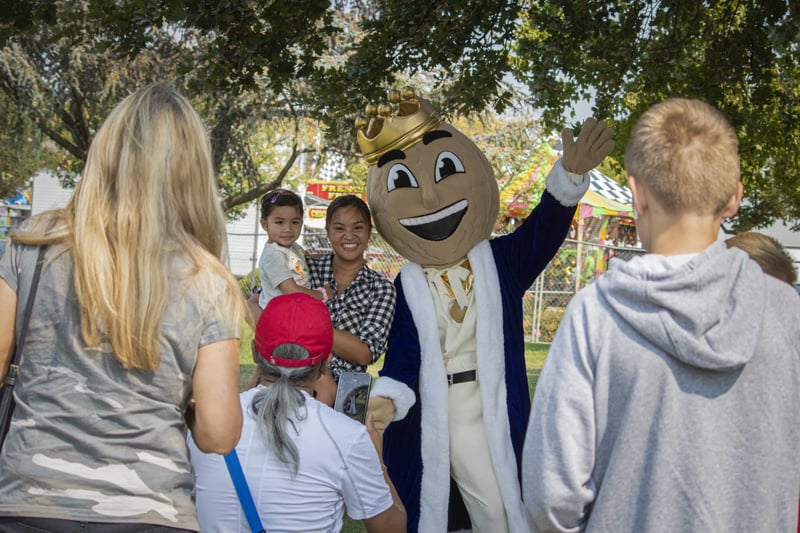 Families enjoying the Walnut Festival in a park, with children posing with the festival mascot and other attendees around them.