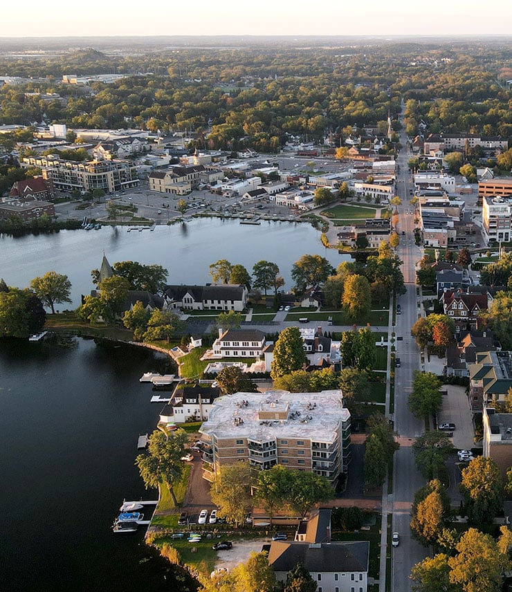 Aerial view of downtown Oconomowoc with buildings, streets, and lakes at sunset