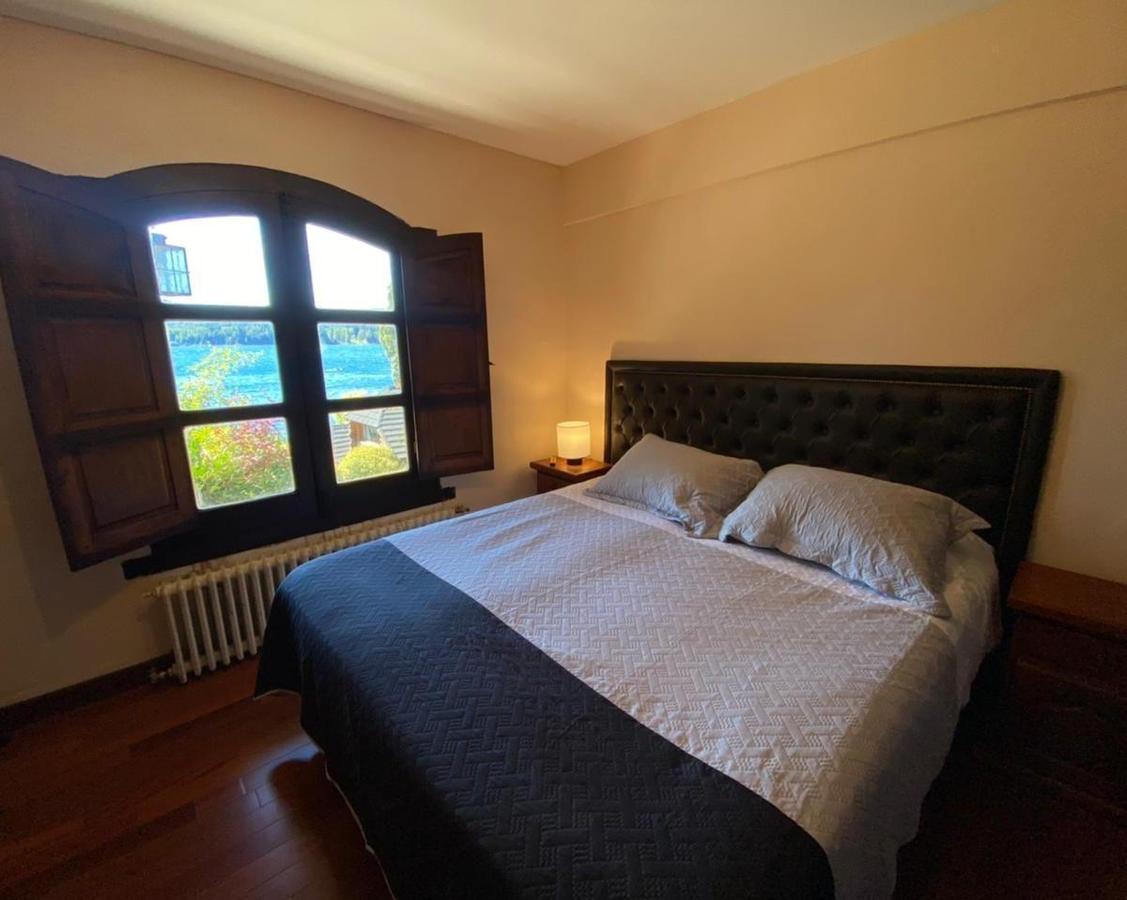 Bedroom with a dark tufted headboard and arched shuttered window overlooking water.