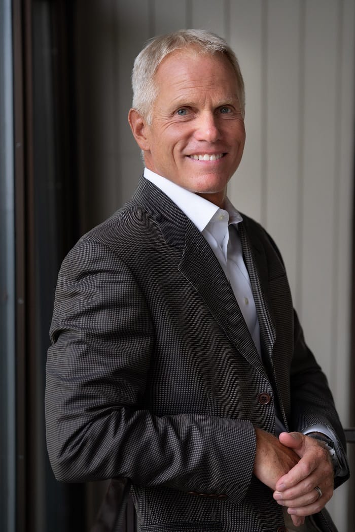 Peter Adams smiling in a dark patterned blazer and white shirt.