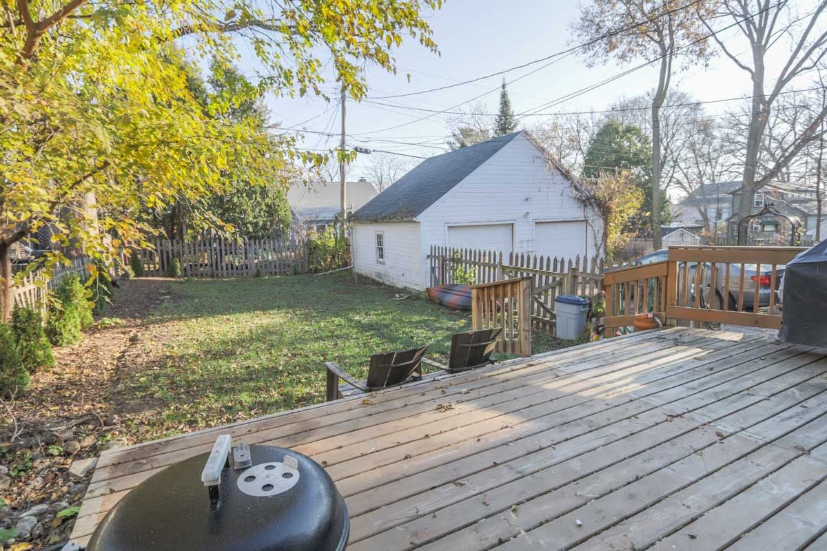 Fenced backyard with a wooden deck, grill, and white detached garage.