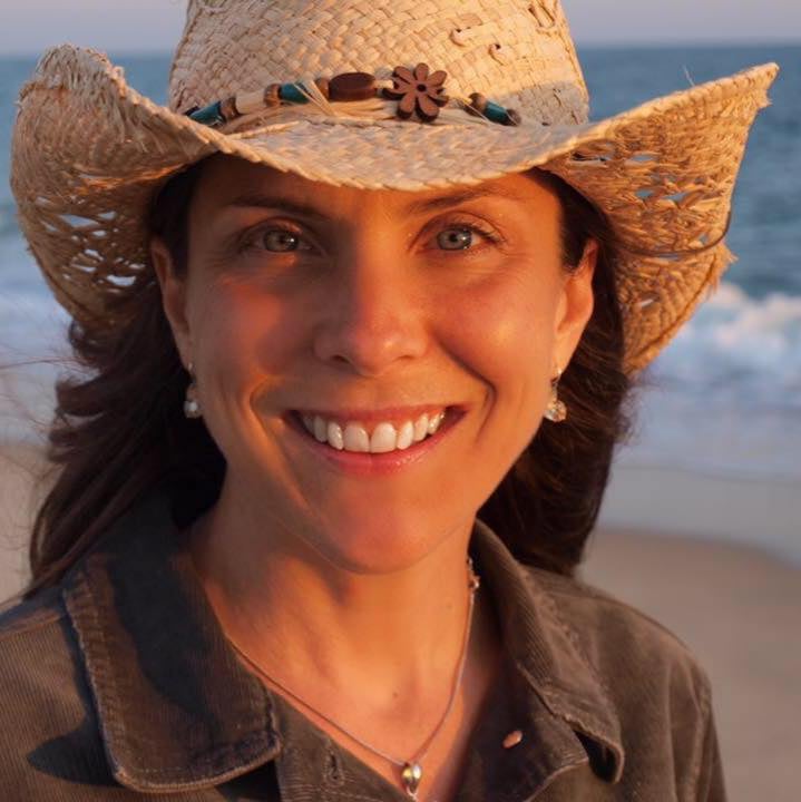 Allyne smiling in a straw cowboy hat by the beach at golden hour.