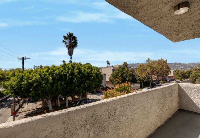 Apartment balcony overlooking a tree-lined neighborhood with distant hills.