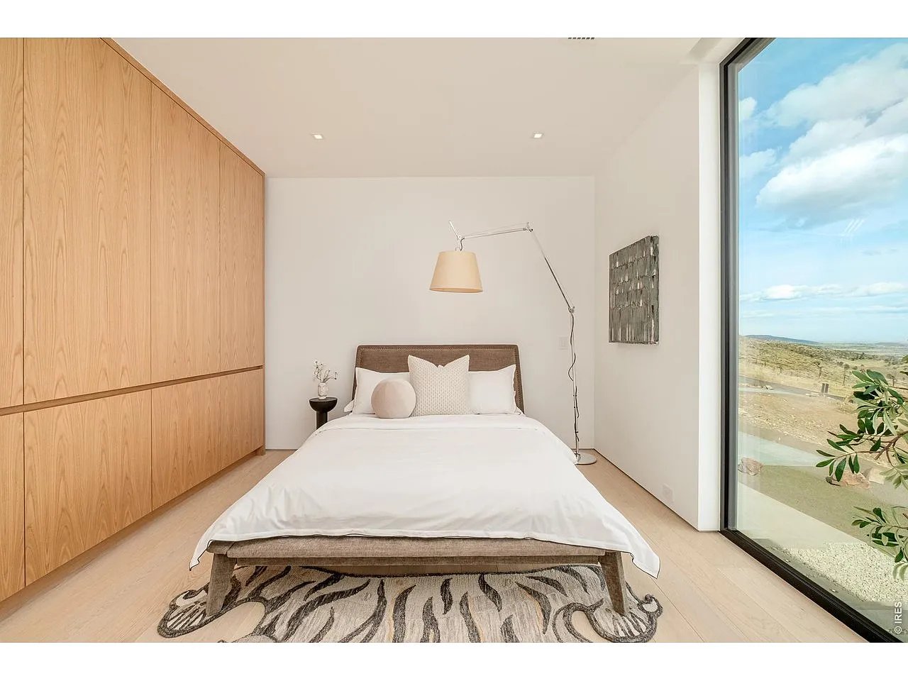 Modern bedroom with built-in wood cabinetry and a floor-to-ceiling window overlooking rolling land.