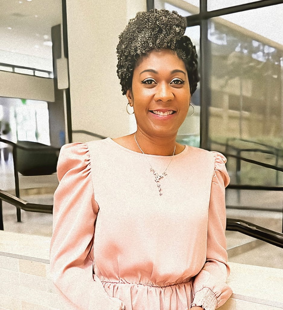 Tiffany Simms smiles in a pale pink dress inside a modern glass-walled office.