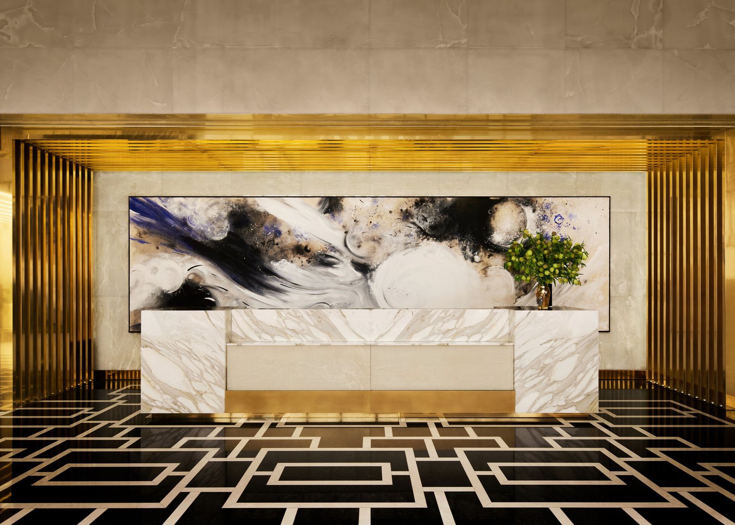 Lobby reception desk with white marble, gold accents, abstract artwork, and a geometric black floor.