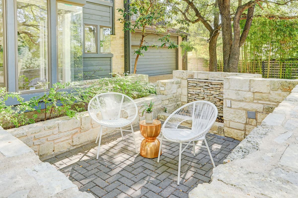 Stacked-stone courtyard seating area near the garage at 2131 Barton Hills Drive, Austin, TX 78704, with a paver patio and woven chairs. Barton Hills neighborhood.