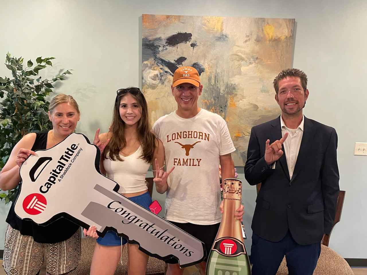 Four people pose with an oversized Capital Title congratulations key and champagne-bottle-shaped prop.