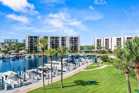 Waterfront condominiums overlooking a marina, with docked boats, palm trees, and a green lawn.