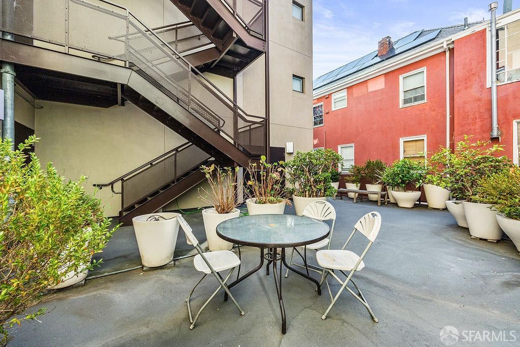 Shared courtyard patio with a round table, folding chairs, potted plants, and an exterior metal staircase.