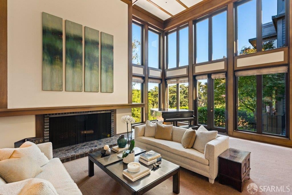 Living room with towering wood-framed windows, a fireplace, grand piano, and cream sofas.