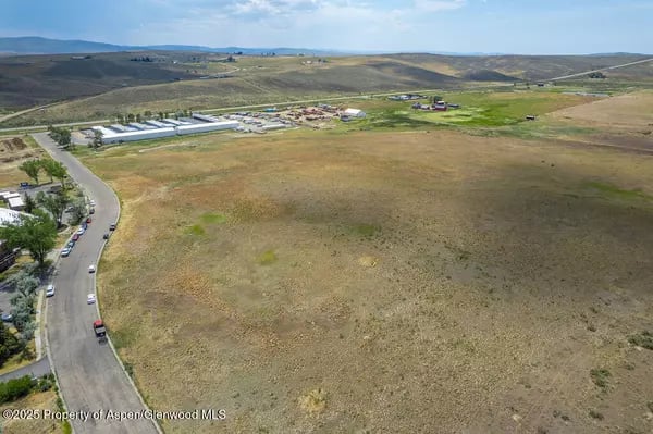 Aerial view of dry open land beside a curving road, low buildings, and rolling hills.