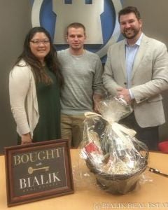 Three adults pose with a wrapped gift basket and a “Bought by Bialik” sign.