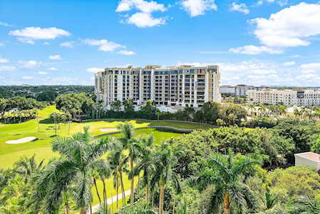 Condominium overlooking a golf course, with palm trees and lush greenery in the foreground.