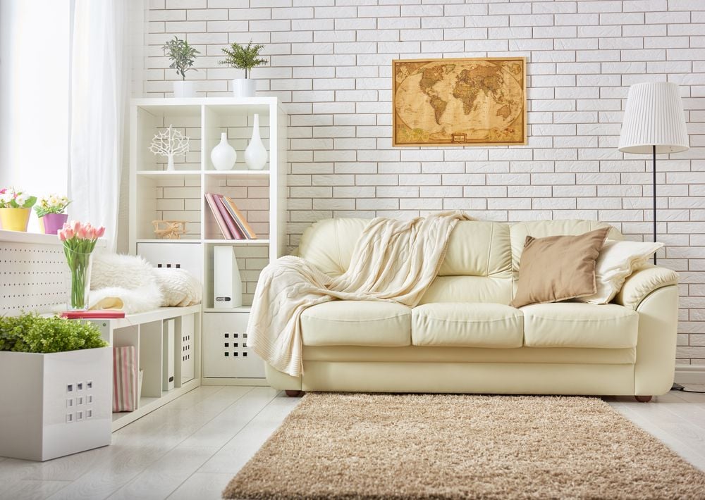 Living room with a cream sofa, white brick wall, framed world map, and beige rug.