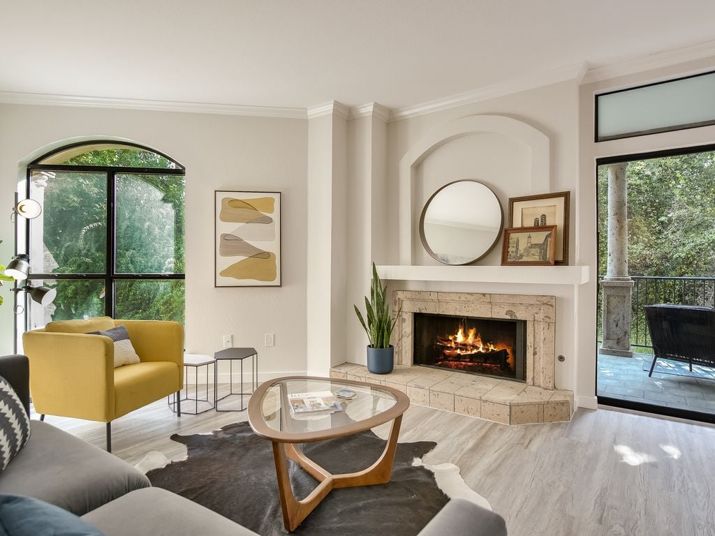Living room with a stone wood-burning fireplace, an arched window, and greenbelt views at 1000 Liberty Park Drive #203, Liberty Park Condominiums, Westlake, Austin, TX 78746.