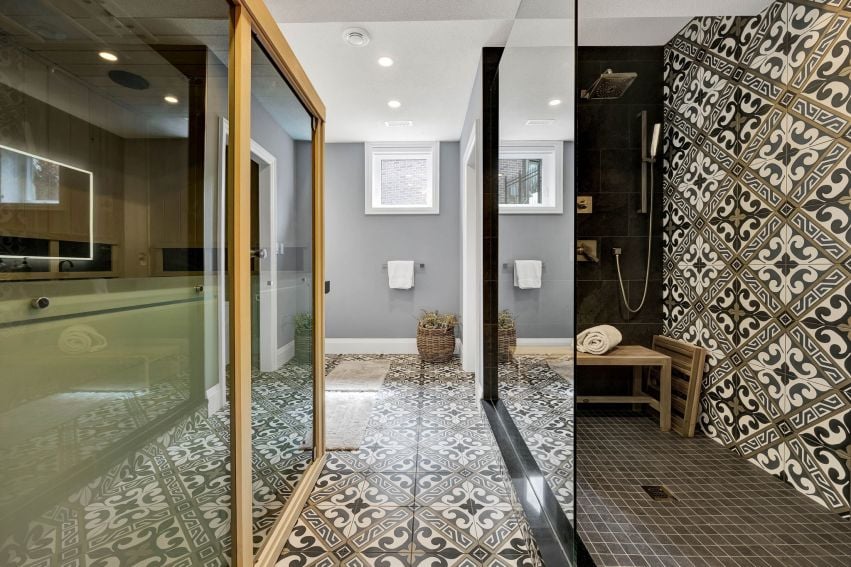Wellness bathroom with a glass-enclosed sauna, black-tiled shower, and ornate patterned tile.