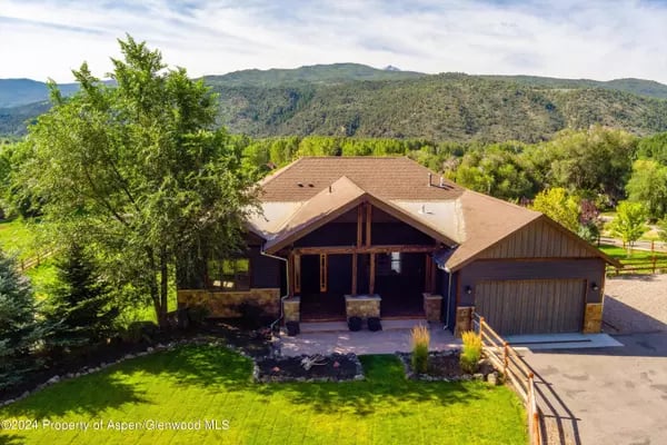 Cerise Ranch home with a covered porch and attached garage, backed by green mountains.