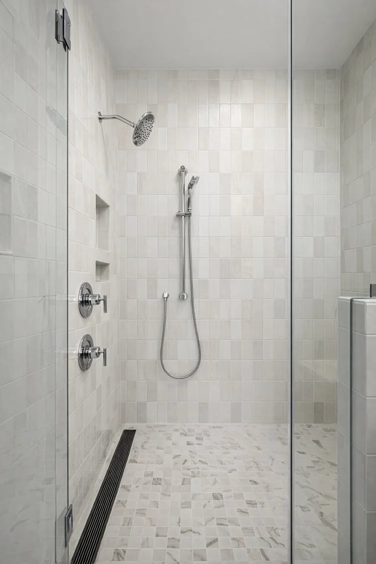 Walk-in shower with white tile, rainfall and handheld showerheads, recessed niches, and a linear floor drain.
