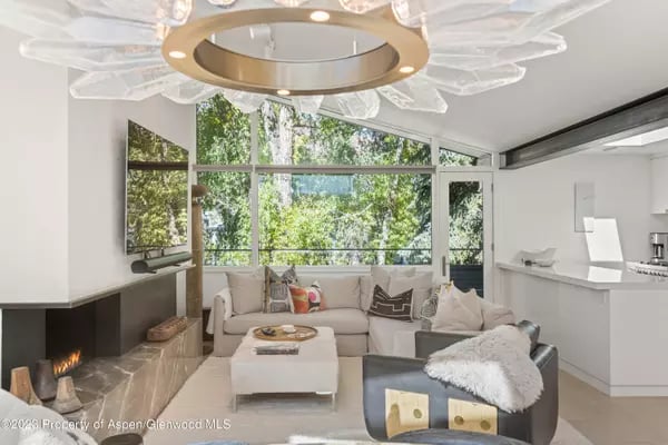 Bright living room with a white sectional, fireplace, and large windows overlooking trees.