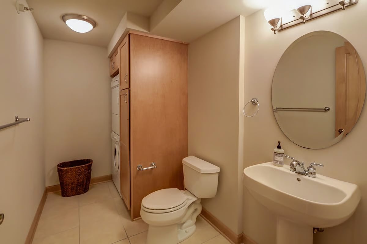Bathroom with a wall-mounted sink, oval mirror, wood cabinetry, and an enclosed laundry appliance.