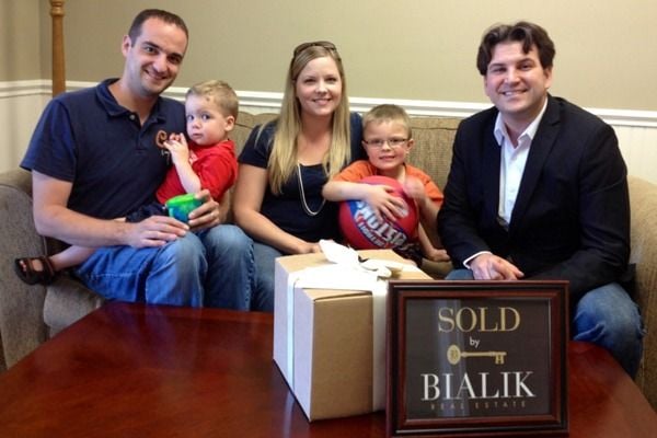 A family with two children celebrates beside a Bialik Real Estate agent and a SOLD sign.