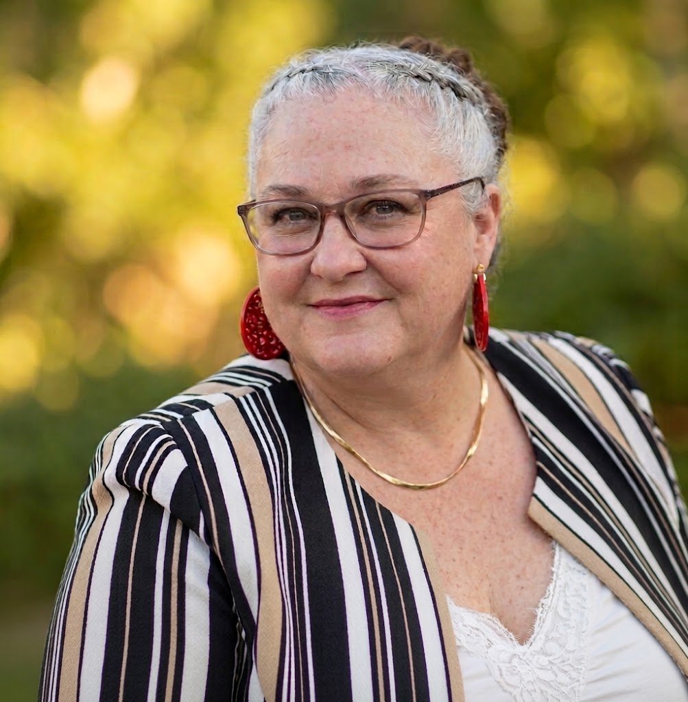 Raechel Stone wearing glasses and red earrings in a striped jacket outdoors.