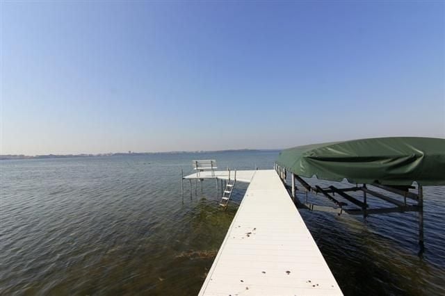 White dock extending into a lake beside a covered boat lift.