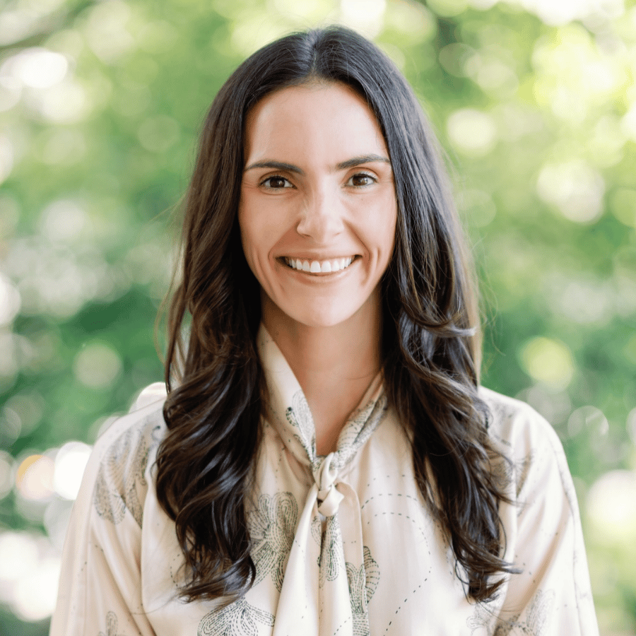 Larson Mitchener smiling in a cream patterned blouse against a blurred green background.