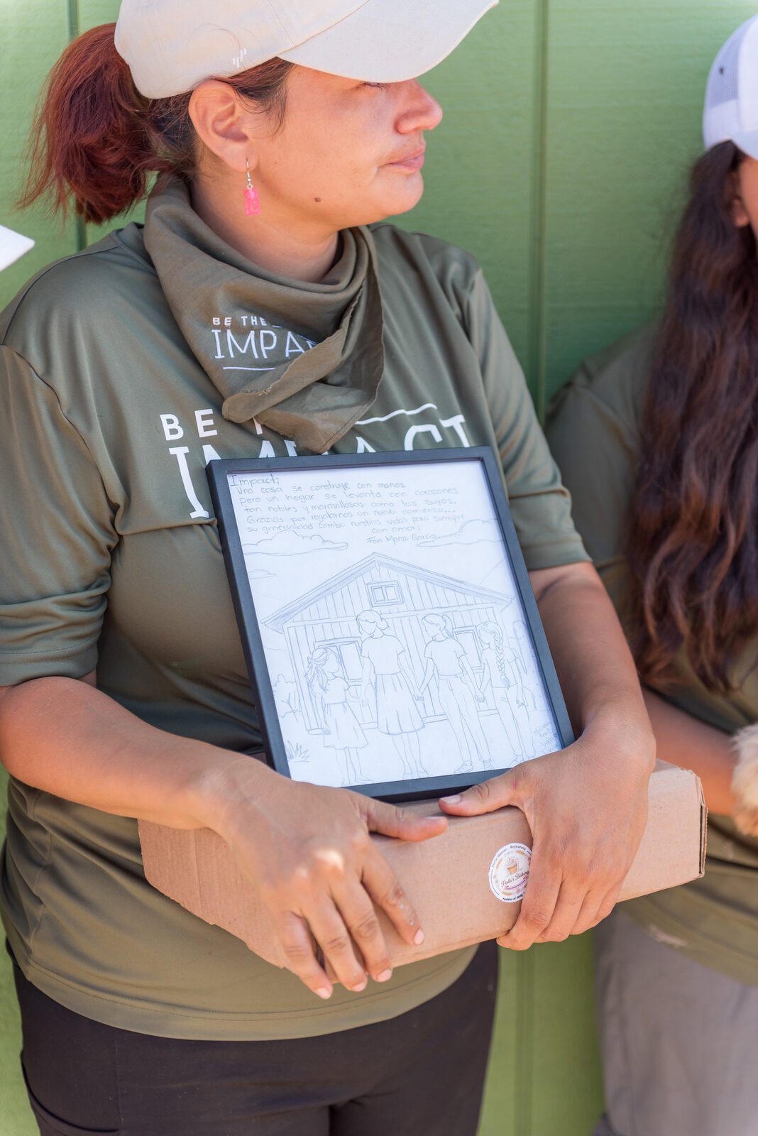 A volunteer holding a framed pencil drawing of the new house with the family standing in front of it, given as a thank-you gift at the handover
