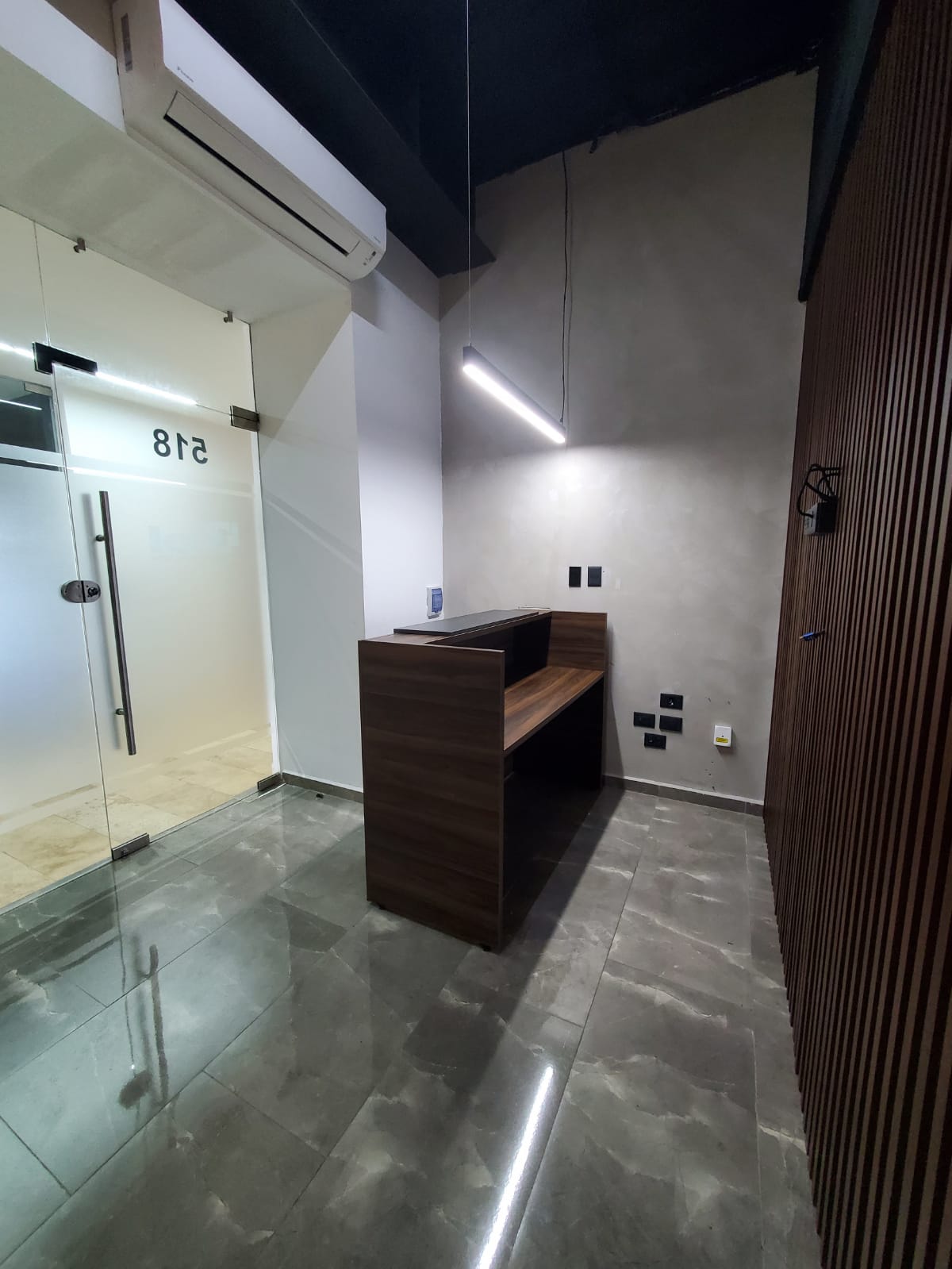Modern office reception with a dark wood desk, glass entrance marked 518, and stone tile flooring.