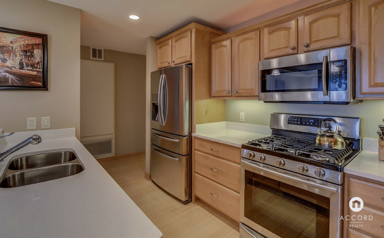 Condo kitchen with stainless steel appliances, light wood cabinets, and a double-basin sink.