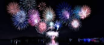 Colorful fireworks burst over water at night, reflected on the surface.