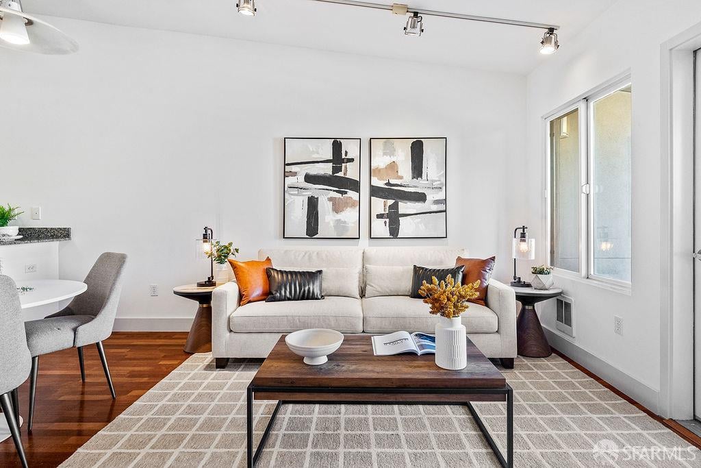 Bright staged living room with a white sofa, abstract art, hardwood floors, and large windows.