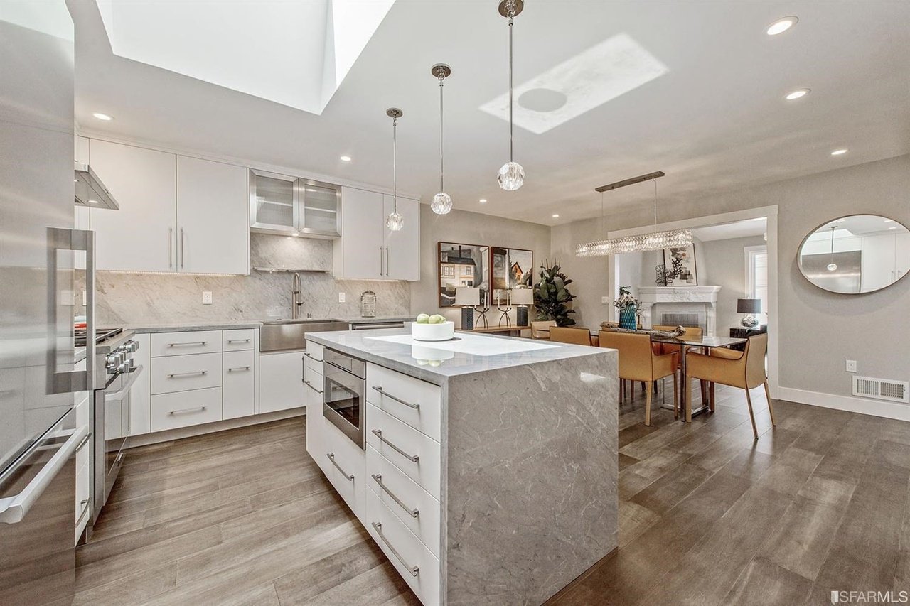 Open-plan kitchen with a large marble island, white cabinetry, and adjoining dining area.