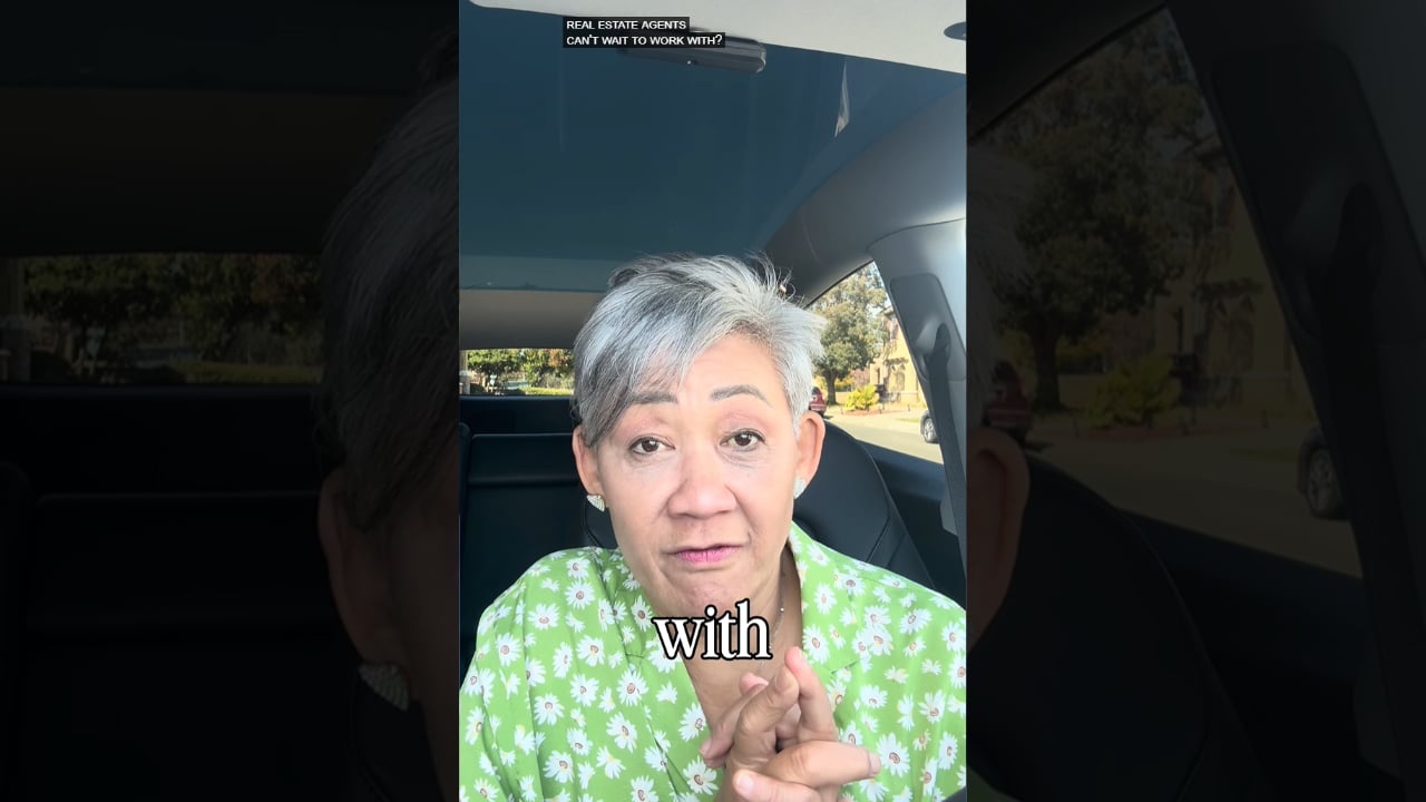 Woman with short gray hair speaking to the camera in a car, wearing a green floral blouse.