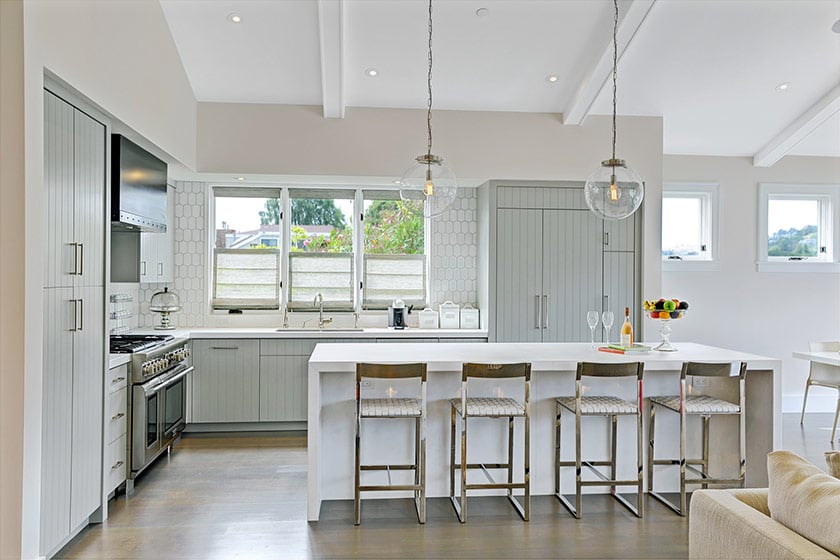 Staged kitchen with gray cabinets, stainless steel appliances, and a white island lined with four bar stools.