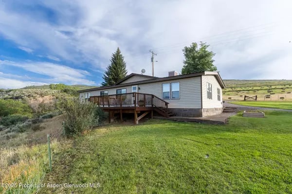 Single-story home with a raised wooden deck and green lawn in a rural setting.