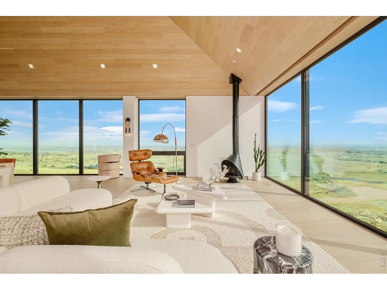 Modern living room with vaulted wood ceiling, wall of windows, black fireplace, and wide countryside views.